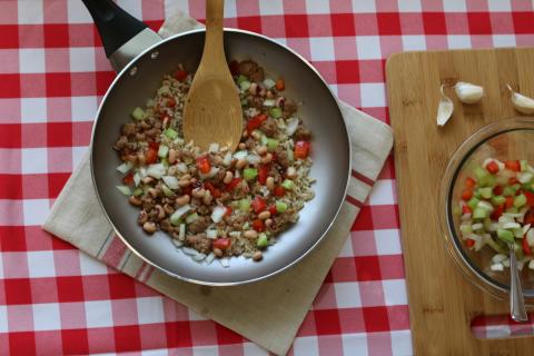 peas and rice in a pan on a white and red checkered tablecloth next to cutting board with chopped veggies
