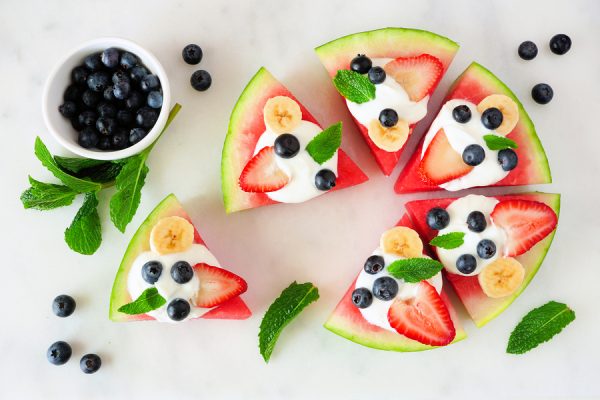 Summer watermelon pizza with blueberries, strawberries, bananas, mint and yogurt. Top view on a marble background.