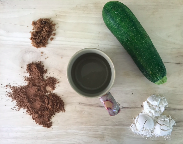 Ingredients for the chocolate zucchini mug cake poured out onto a wooden slab around an empty mug