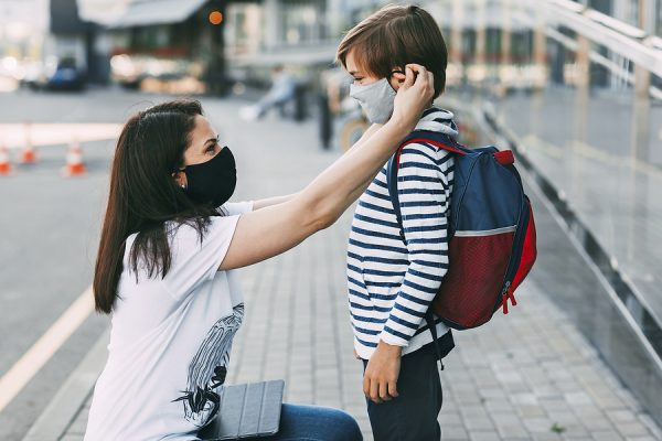 Mother adjusts her sons mask on the sidewalk during the coronavirus pandemic.