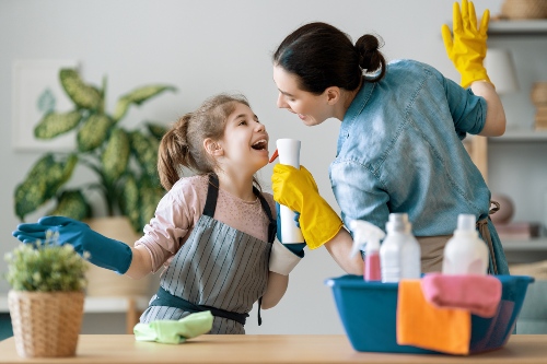 Mother and daughter sing into cleaning supply bottles while wearing cleaning gloves and aprons