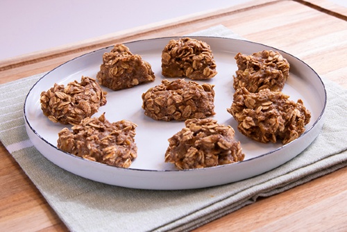 Plate of oatmeal drop cookies sits atop a napkin and wooden board