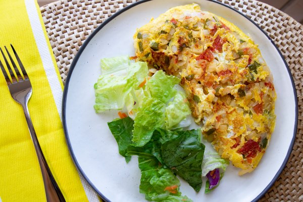 Omelet sits on a white plate next to a green salad.There is a fork on a yellow napkin beside the plate.