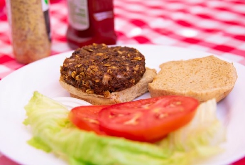 black bean burger sits atop an open face bun with lettuce and tomato on the plate