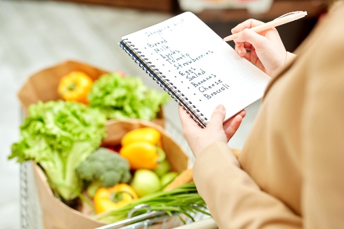 Woman checking food items off of grocery list with bags of produce in background