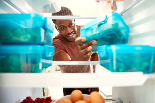 Man grabbing a blue tupperware of meal prepped food out of the fridge