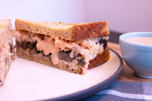 Half of a mushroom sandwich with cheese and dressing dripping down the side