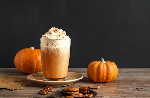 Pumpkin spice latte topped with whipped cream and surrounded by mini pumpkins