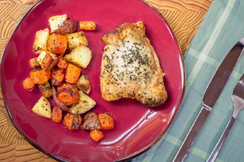 Red plate with a seasoned chicken thigh and pile of seasoned carrots and potatoes