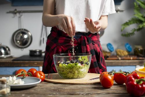 woman adding seasoning to salad