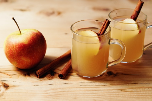 Apple cider in clear mugs with apple slides and a cinnamon stick