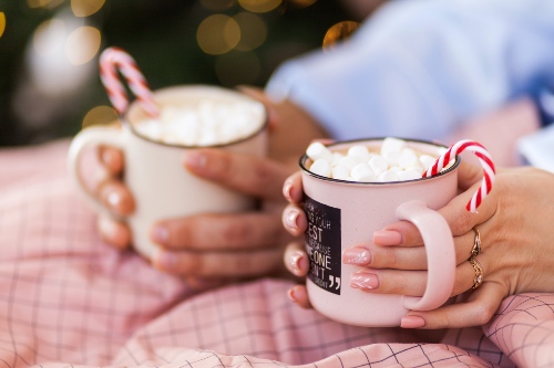 Couple sitting under a blanket both holding mugs of hot chocolate with candy canes