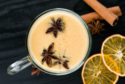 Mug with hot tea and milk with cinnamon sticks and lemon slices on the side