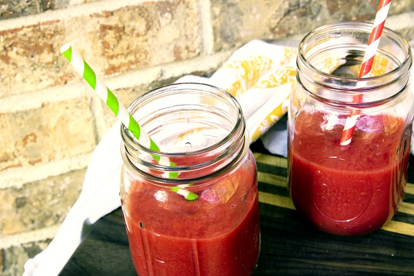 Two mason jars of a bright fuschia drink with bright striped straws sit on a dark table with a brick background