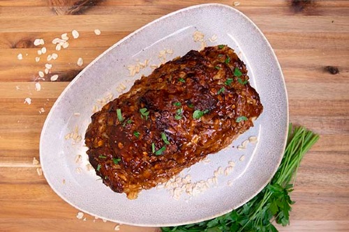 Baked meatloaf sits on an asymmetrical plate surrounded by parsley and oats