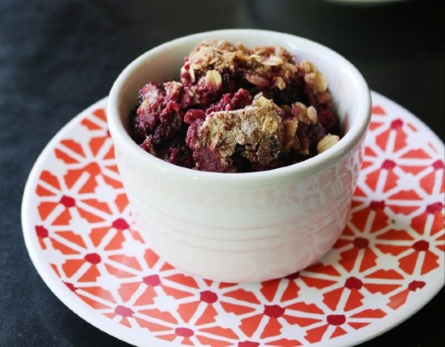 Photo shows a white bowl of fruit and crisp topping sitting on a red patterned plate.