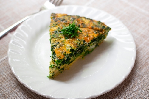 Slice of yellow and green frittata sits on a white plate