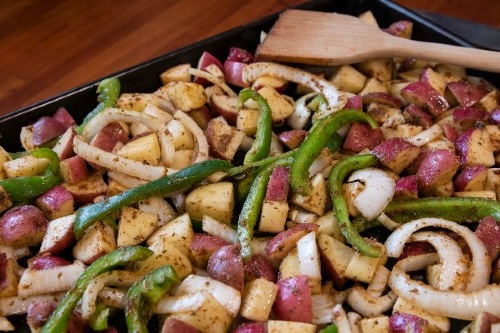 Sheet pan of red potatoes, green bell peppers, and onion slices covered in seasonings