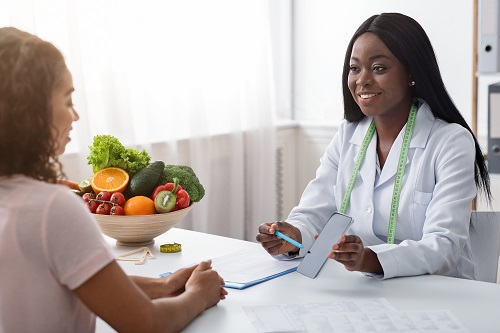 Two women sitting across from each other as one shows something on her phone. Bowl of fruit in background.