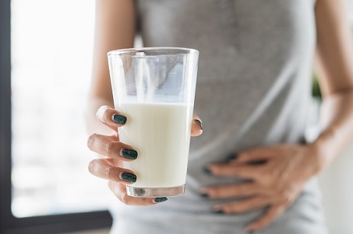 Woman holding a glass of milk and having a stomachache.