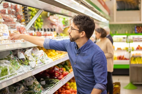 Man in blue shirt picking out vegetables off a grocery store display