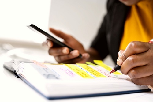 hands holding phone and writing in a planner with sticky tabs