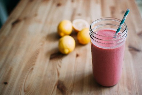 Strawberry smoothie in a glass jar with lemons in the background