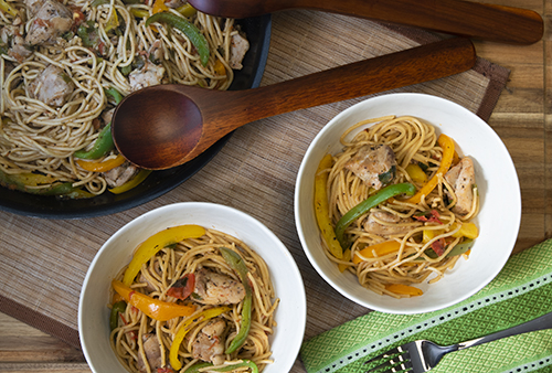 Two bowls and a skillet of spaghetti noodle dish with pieces of chicken and colorful vegetables