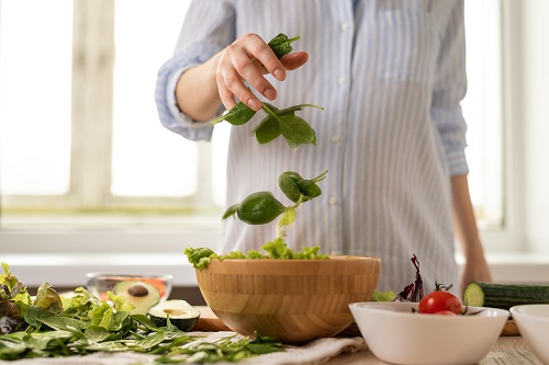 close up pregnant woman in blue shirt assembling a salad with spinach leaves