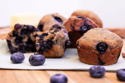 buttermilk blueberry muffins sitting on a wooden cutting board with fresh blueberries scattered around