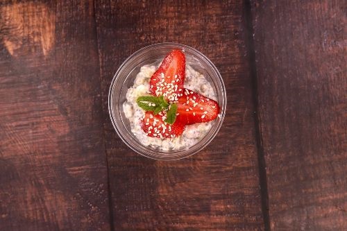 glass bowl with cream and strawberries on top on a wooden table