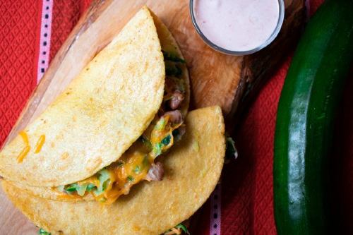 quesadillas with a side dish of zesty sauce and a fresh, whole zucchini laying beside the plate 