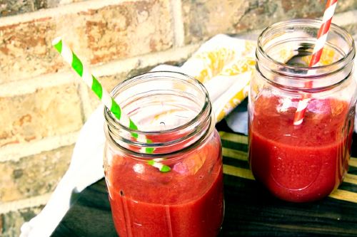 two mason glasses with a bright red colored fruit and veggie drink 