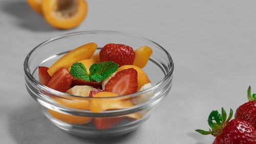 mixed fruit in a glass bowl with strawberries on the side