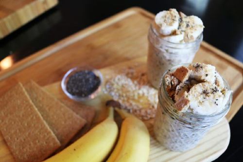 banana pudding overnight oats in a jar on a wooden cutting board with bananas and chia seeds placed around it