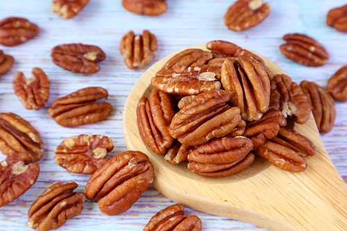 Wooden Spoon Full of Pecan Nuts with Many Scattered on Pale Blue Wooden Table