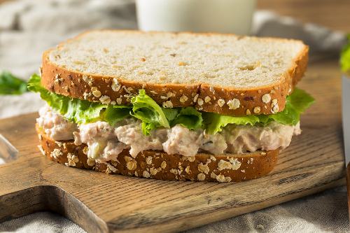 tuna salad sandwich sitting on top of a wooden cutting board 