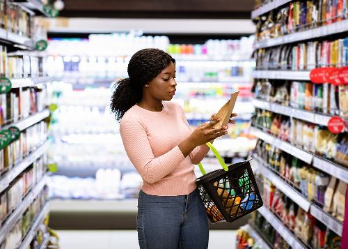 young female shopping in a grocery store aisle reading a food label 