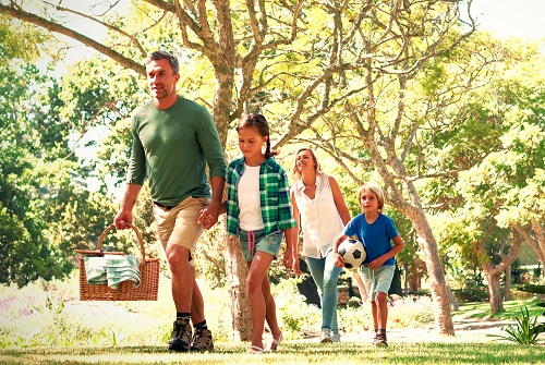 Family arriving in the park for picnic on a sunny day with a picnic basket and a soccer ball