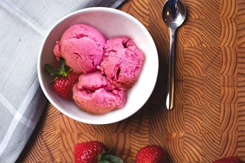 White bowl on a wooden board filled with pink scoops of strawberry frozen yogurt. 