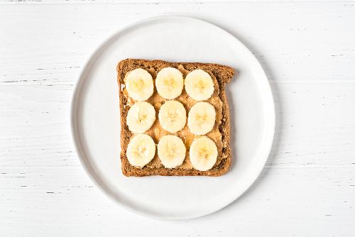 a slice of whole grain toast with banana slices and peanut butter sitting on a white plate