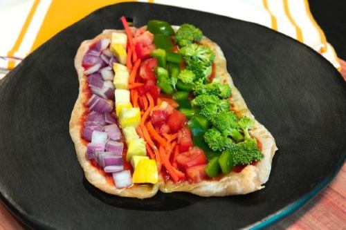 flatbread pizza with a rainbow of fresh vegetables on top on a black plate with a gold and white striped napkin in the background