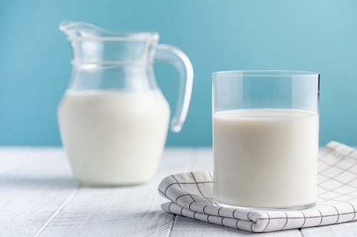 Glass and pitcher of milk on blue background
