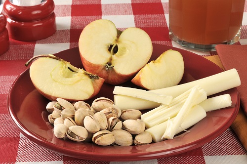 a healthy snack with pistachios string cheese apples and a glass of juice