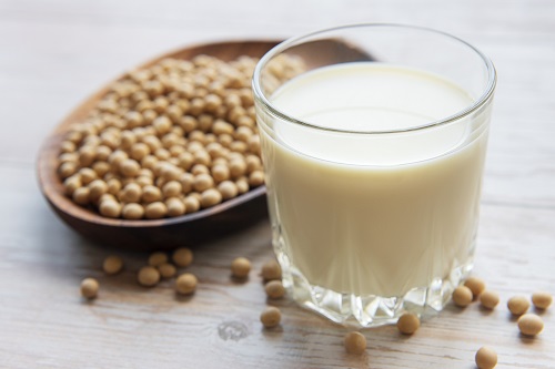 glass of soymilk and bowl of dried soybeans on a table
