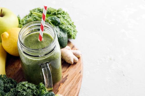 green smoothie in a glass jar surrounded by fresh green ingredients