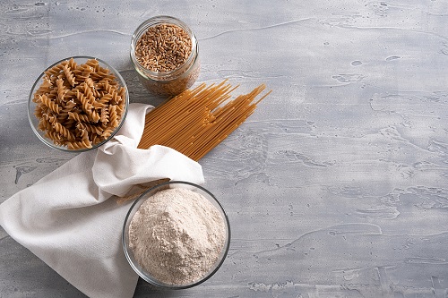 whole grain pasta and flour in bowls and a bag on a gray background