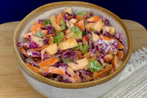 apple coleslaw in a bowl on a wooden cutting board