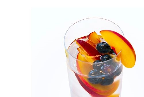 peaches and blueberries in water in a clear glass on a white backgorund