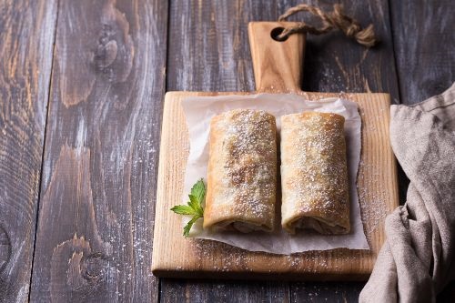 2 rolled tortillas on a white cloth on top of a wooden cutting on a wooden counter with a towel beside the cutting board